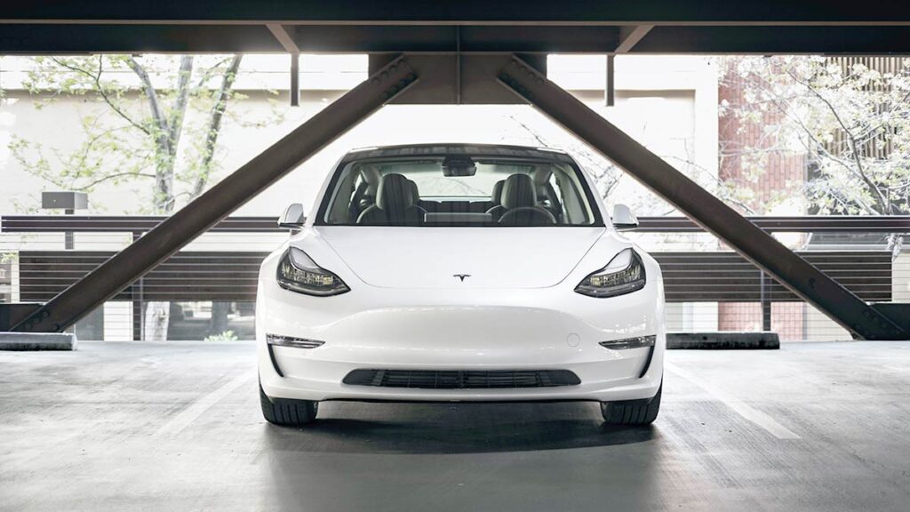 White Tesla Model 3 standing in front of the garage.