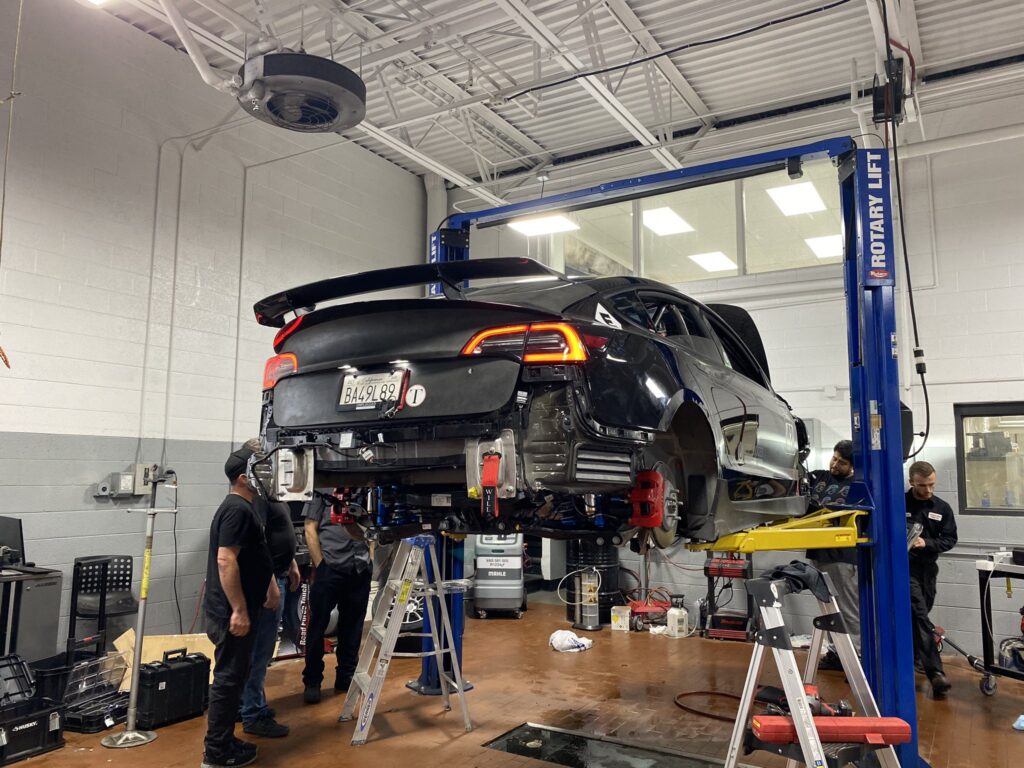 Unplugged Tesla Model 3 Performance (CORSA 42) on the workshop lift, getting extensive repairs and parts replacement (rear view).