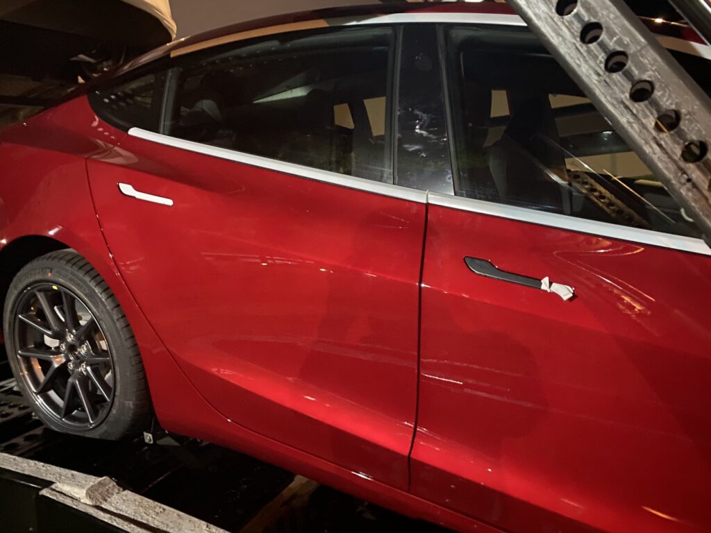 Chrome deleted window trim and door handles seen on a red Tesla Model 3.