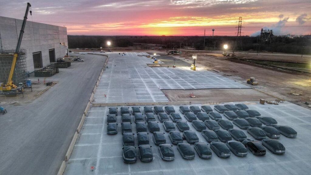 More than 50 first-production Giga Texas-made Tesla Model Y electric SUVs parked outside the production building.
