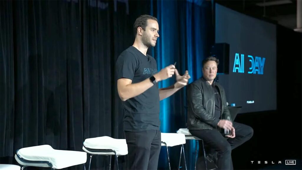 Director of Artificial Intelligence at Tesla Andrej Karpathy giving Tesla AI Day presentation (2021), Elon Musk sitting and listening in the background.