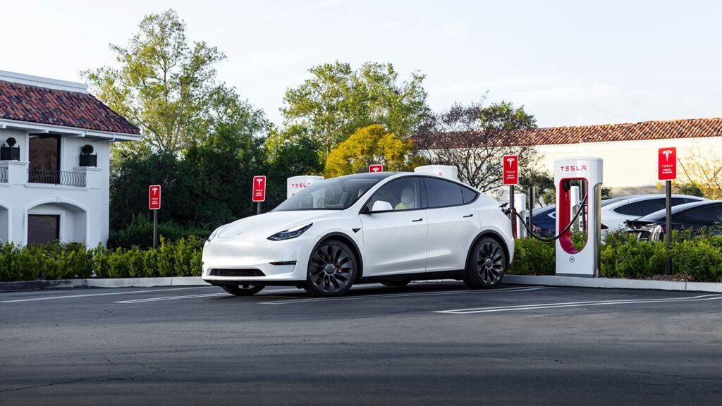 A white Tesla Model Y charging at a Supercharger.
