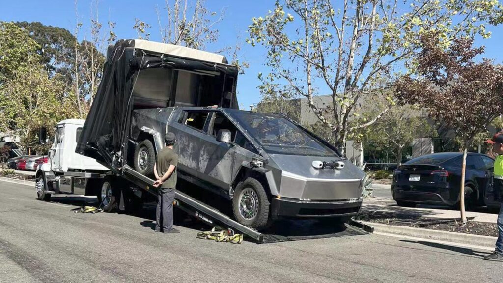 Tesla Cybertruck getting unloaded from a covered tow truck in California after a hard day of testing. Cameras, sensors, and wheel force transducers installed for testing are visible.