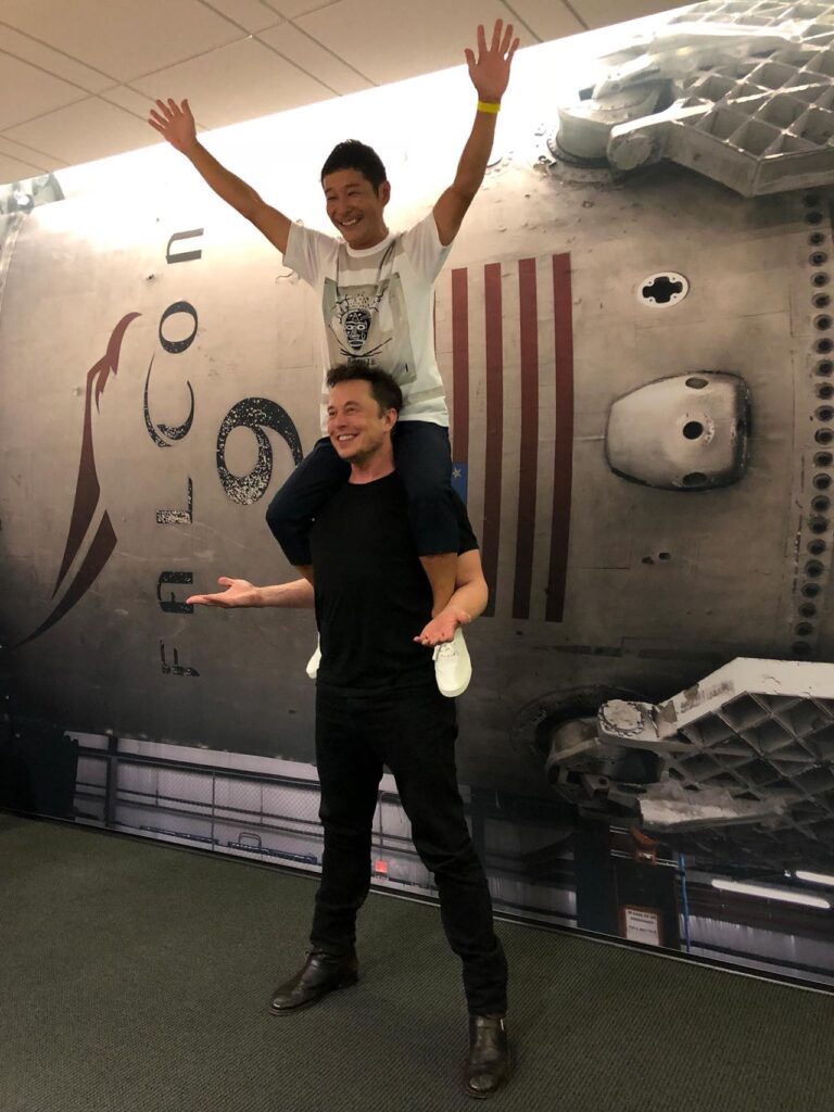 Japanese billionaire entrepreneur and dearMoon crew leader Yusaku Maezawa sitting on the shoulders of Elon Musk at the SpaceX HQ in Hawthorne, California.