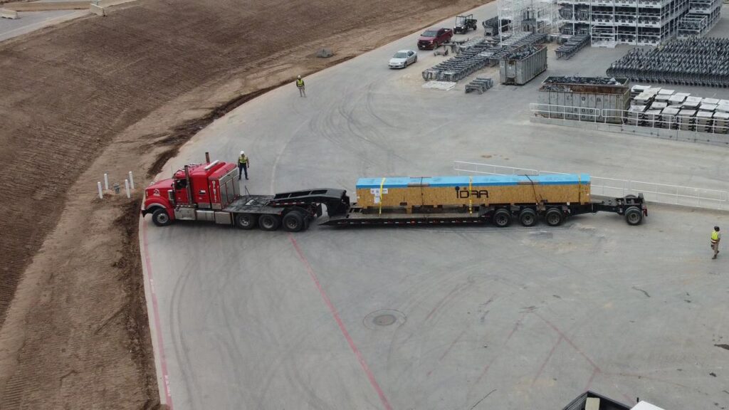 A large part of the IDRA 9000-ton Cybertruck Giga Casting machine arrives at Giga Texas on a long trailer.