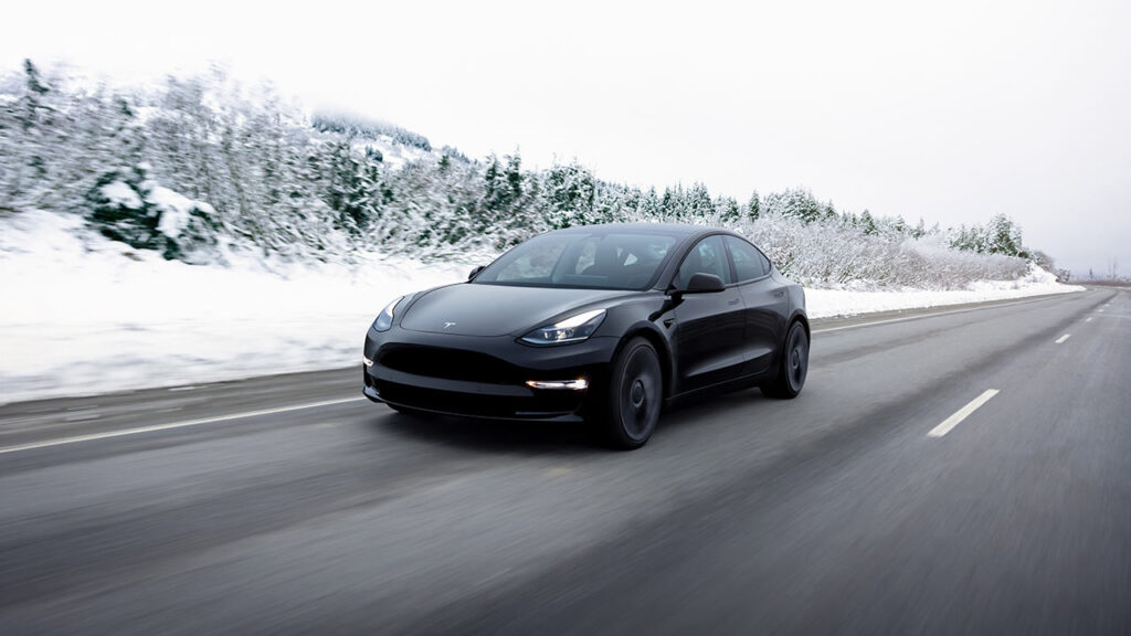 A Tesla Model 3 in black color accelerating on the highway as snow covers the sides of the road.
