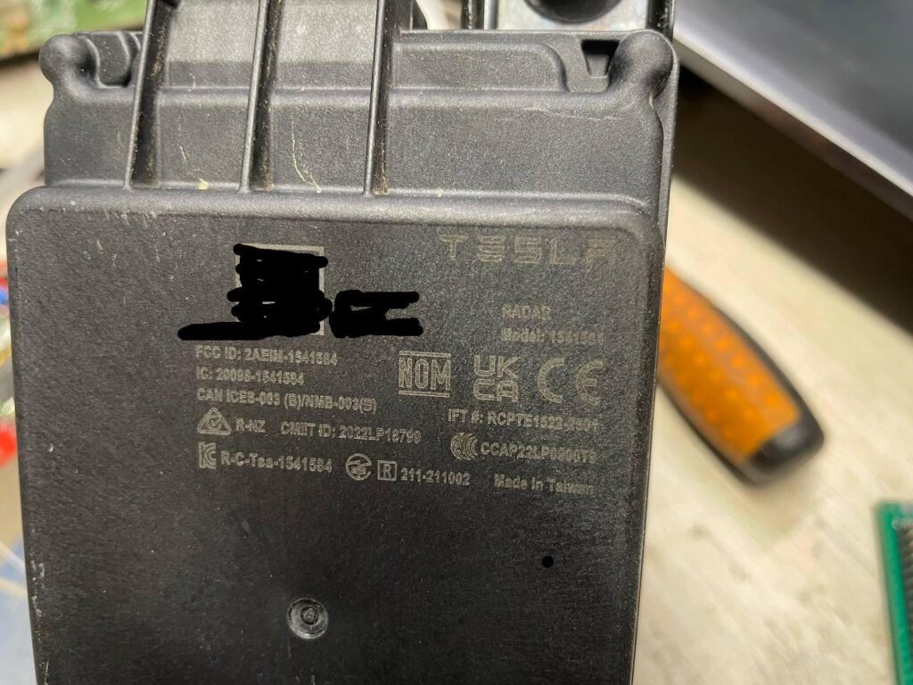 Closeup picture of the Tesla HW4 Autopilot radar that shows the FCC and other compliance information and other labels.
