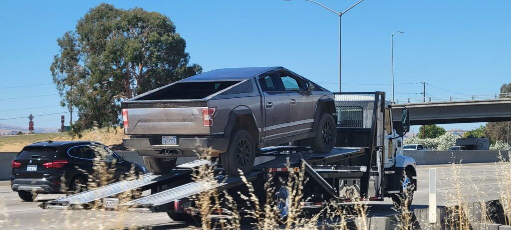Tesla Cybertruck prototype wrapped in a Ford F-150 skin spotted on a tow truck trailer, perhaps leaving California.
