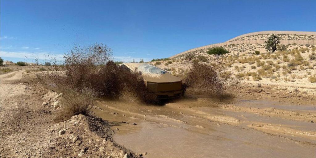 Tesla Cybertruck off-roading in a muddy plane of a desert.