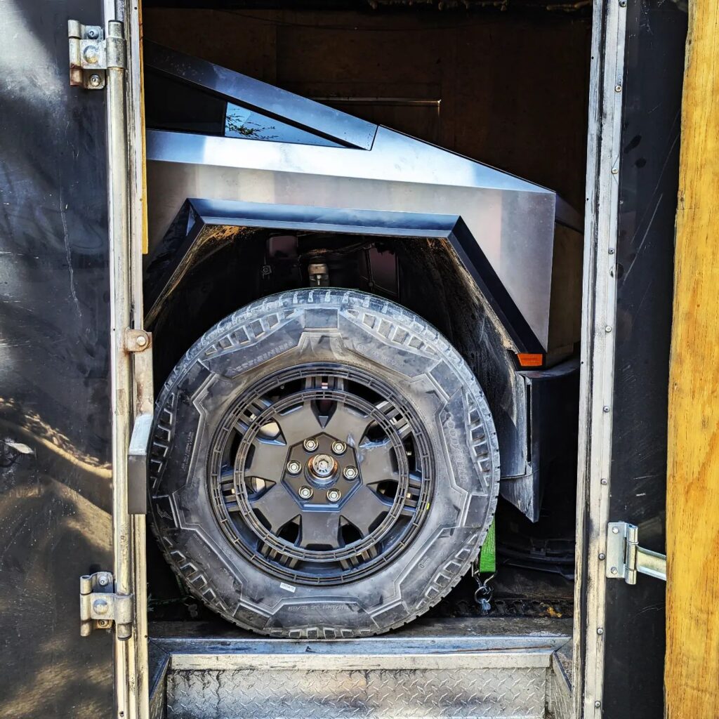 Tesla Cybertruck wheel and side of the front become visible as the door of the enclosed trailer opens.