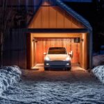 A Tesla Model Y parked in a garage in extreme cold weather as thick snow covers the surroundings of the house.