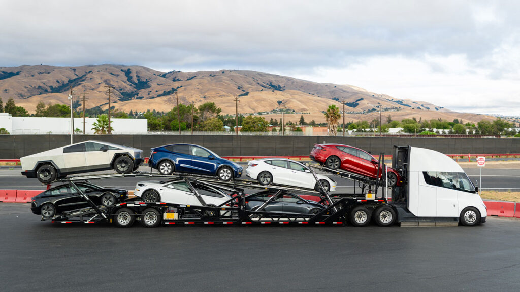 A Tesla Semi truck with a car carrier trailer loaded with Model Y, Model 3, Model S, and a Cybertruck.