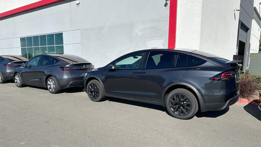 A Stealth Grey Tesla Model X parked behind a Tesla Model 3 in Midnight Silver Metallic color at a Tesla Store.