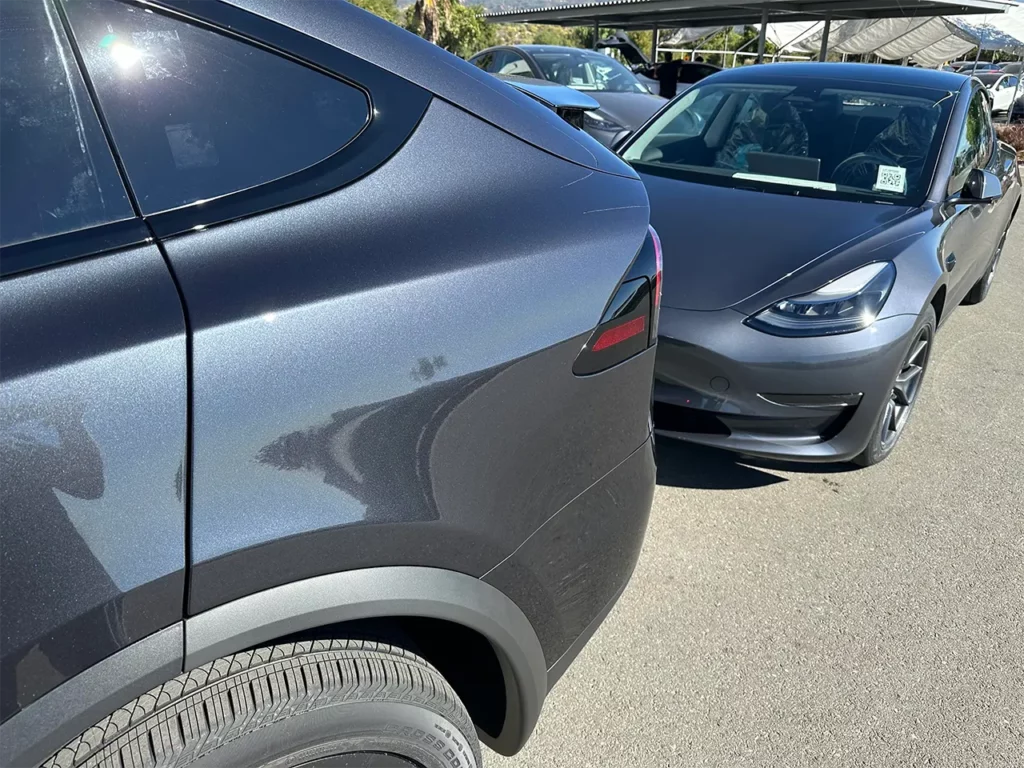 Tesla Model X (front) in Stealth Grey color and a Tesla Model 3 (behind) in Midnight Silver Metallic paint parked outside a Tesla Store.