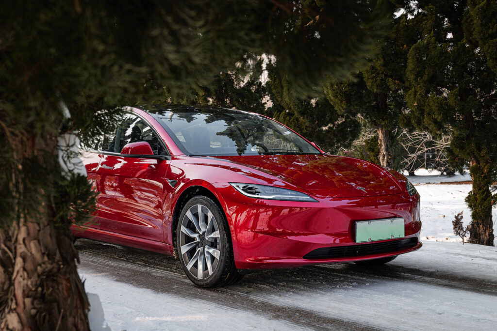 A Tesla Model 3 Highland in Ultra Red color roaming the snowy woods. 