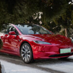 A Tesla Model 3 Highland in Ultra Red color roaming the snowy woods.