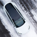 Aerial view of a white Tesla Model Y on a snowy road.