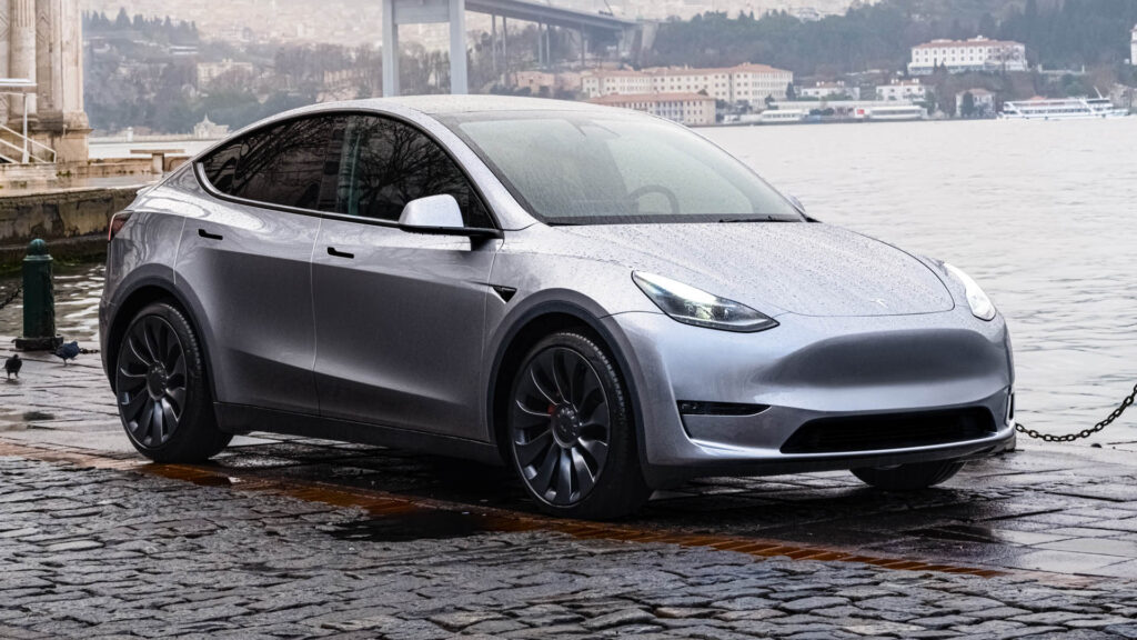Tesla Model Y in Quicksilver color parked on a river bank with water droplets can be seen on its front trunk (frunk) cover.