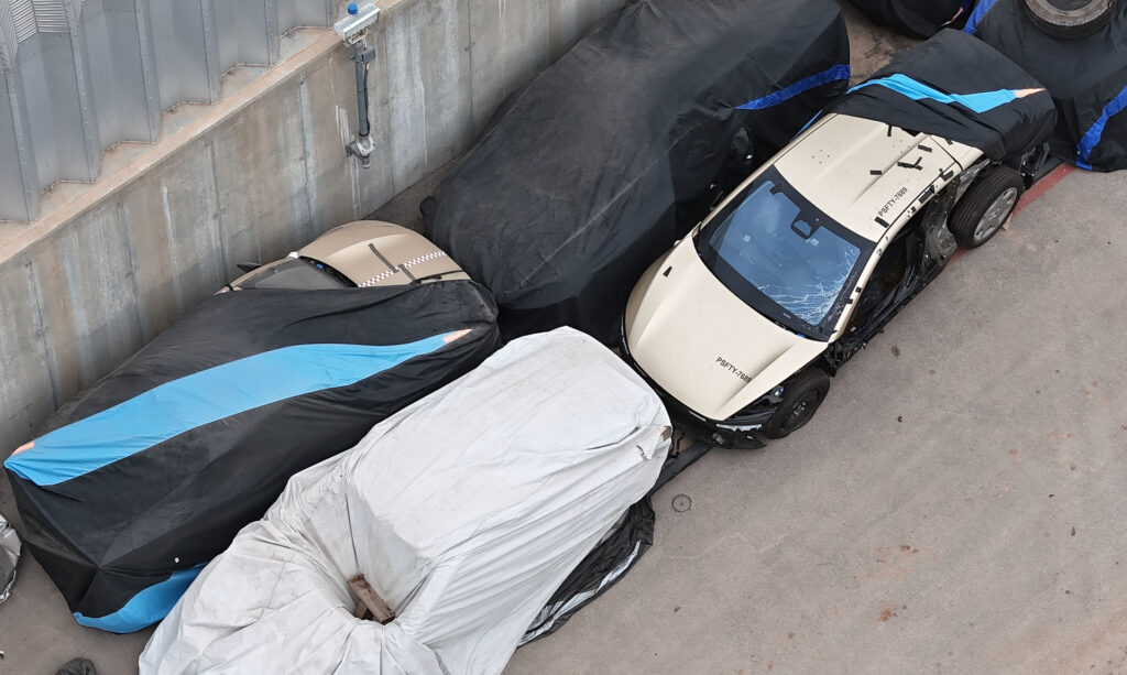 Aerial drone shot of a Giga Texas storage lot showing multiple Tesla Cybercab robotaxis post crash safety testing.