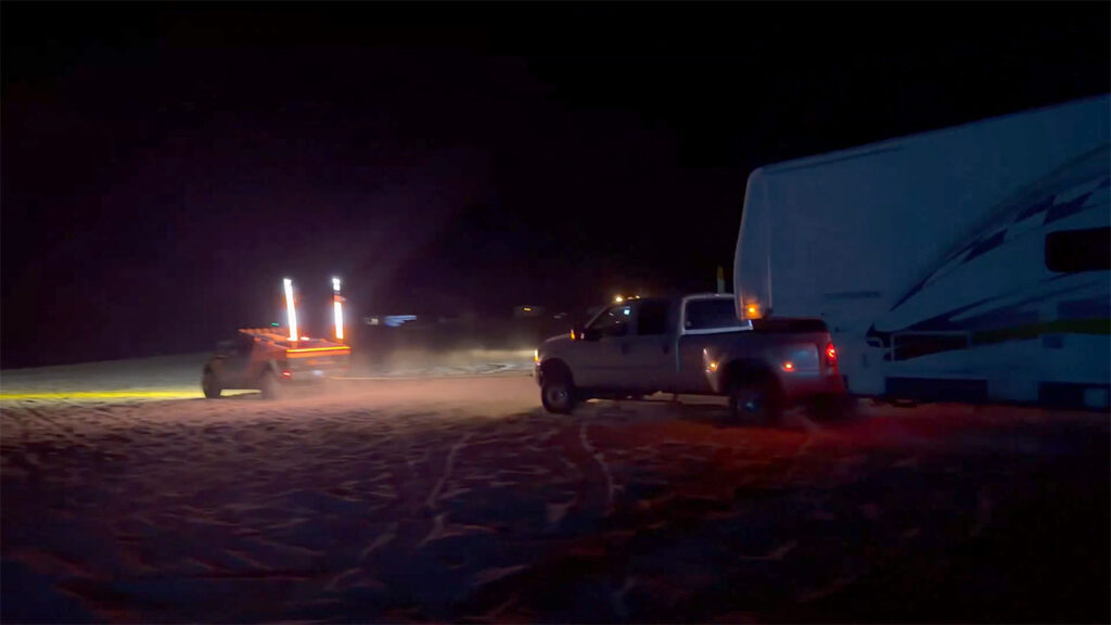 Screenshot from a video showing a Tesla Cybertruck towing an F-350 truck plus a large camping trailer out of deep sand.