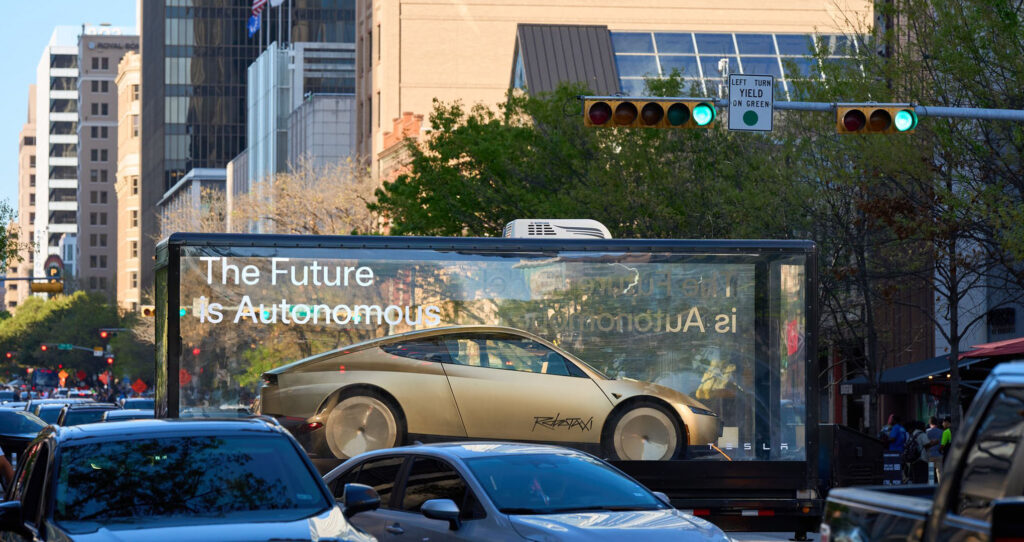 Tesla Cybercab robotaxi vehicle in a mobile glass showcase on a display tour in the United States. Tesla slogan says, "The Future is Autonomous".