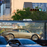 Tesla Cybercab robotaxi vehicle in a mobile glass showcase on a display tour in the United States. Tesla slogan says, "The Future is Autonomous".