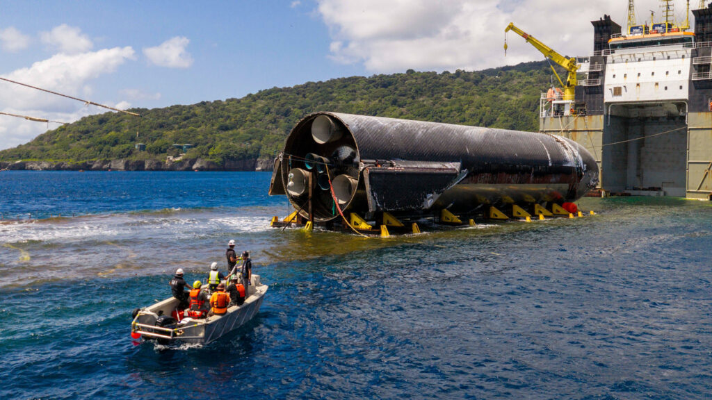 Flight 13 Starship 40 being loaded onto a semi-submersible ship (Forte) as SpaceX engineers monitor it from a distance on a small boat.