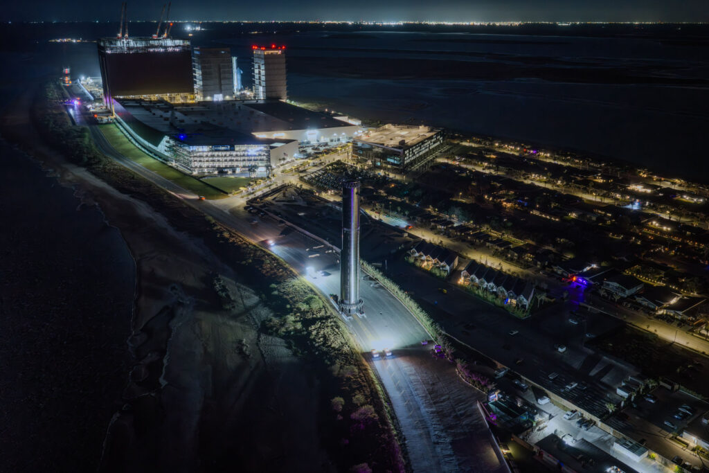 An aerial view of SpaceX Starbase, Texas, showing the Mega Bays, the Starfactory in the background as Booster 41 leaves the production site toward the launch pad.