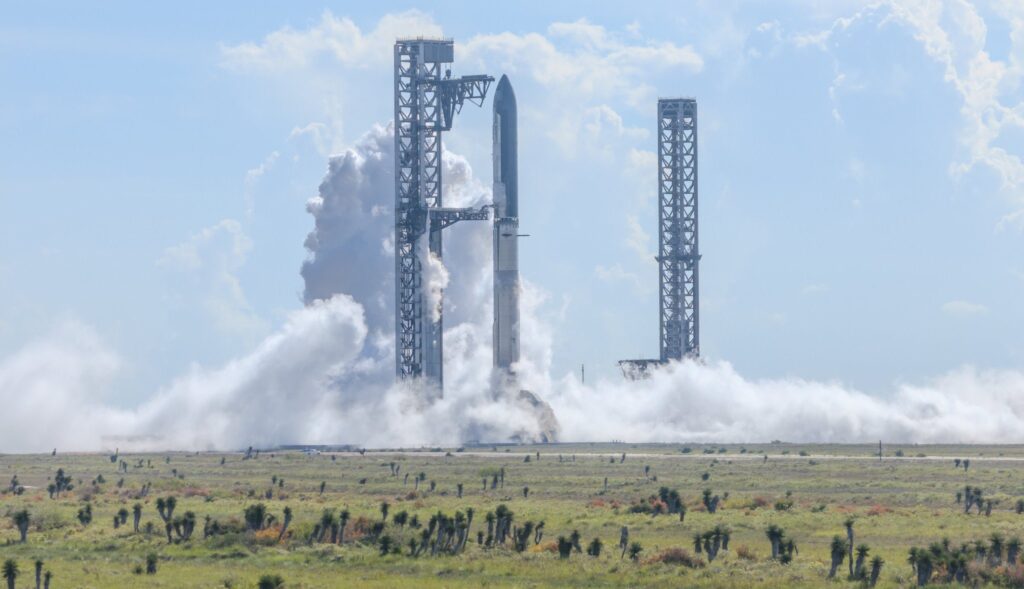 Fully stacked Flight 14 Starship mounted on OLP-2 and held by the launch tower Chopsticks and the redeveloped OLP-1 launch tower can is visible in the background (Starbase, Texas).