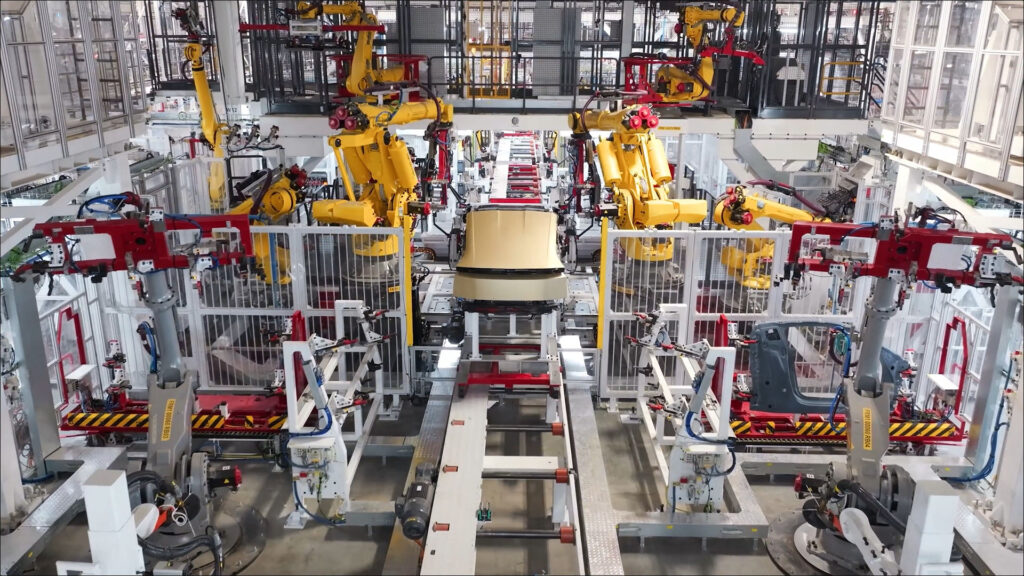 A Tesla Cybercab moving towards the end of the production line as robots have finally attached the body panels after module integration.