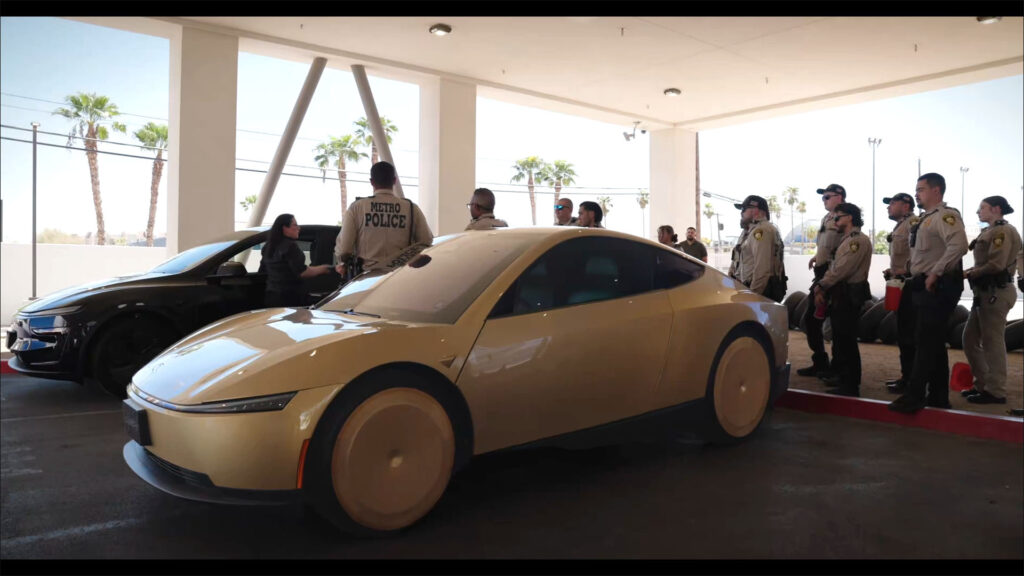 A Tesla Cybercab and a Model Y Robotaxi parked side-by-side as a Tesla executive briefs Austin Metro Police on safety and emergency features of the self-driving vehicles.