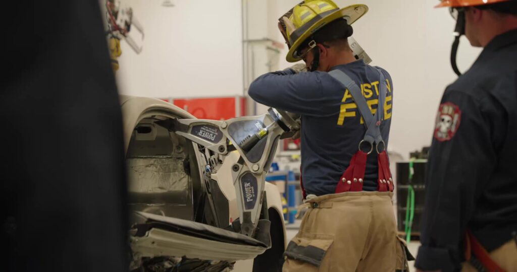 Fire safety first responder using a power tool to open a crashed Tesla Robotaxi.